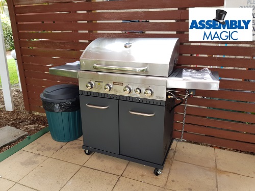 Four burner stainless steel BBQ with Assembly Magic logo in top right corner